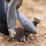 Macro detail of the auger pilot point and carbide cutting teeth packed with soil