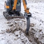 Frost ripper mounted on a mini excavator breaking up a line of frozen ground