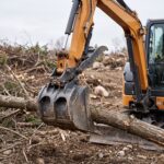 Hydraulic thumb mounted on a mini excavator gripping a tree branch against the bucket